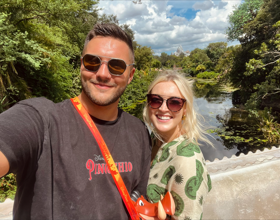 A couple smiling in front of a lush landscape at Disney\u2019s Animal Kingdom, with a view of Expedition Everest in the distance.