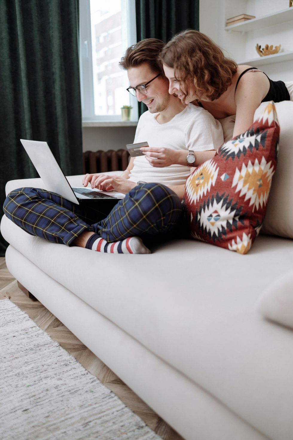 A couple with a credit card on a couch smile at a computer screen.