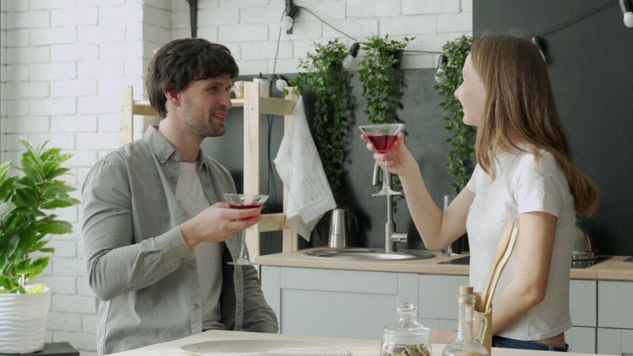 A couple with cocktails in their kitchen.