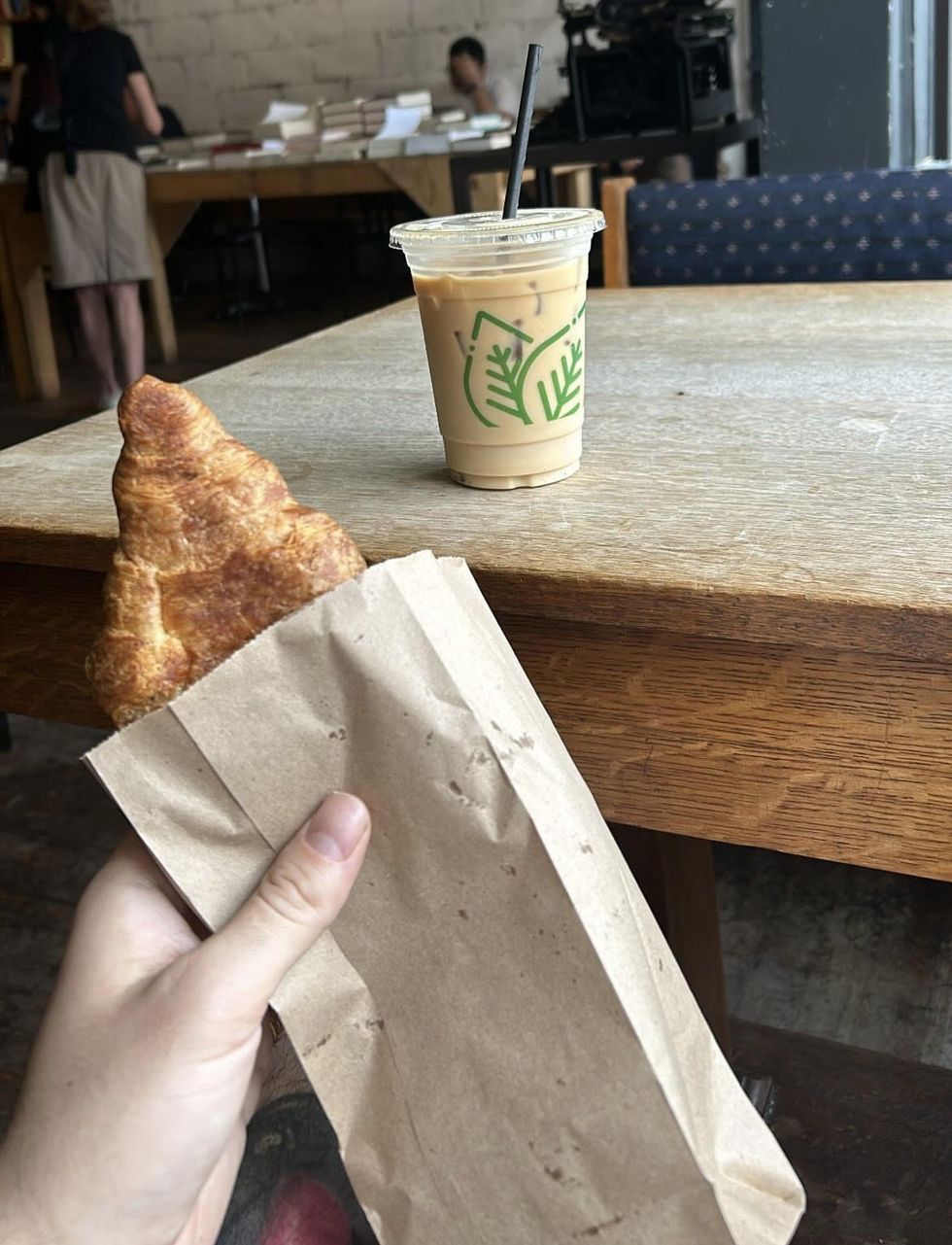 A croissant and an iced coffee in front of a table of books.