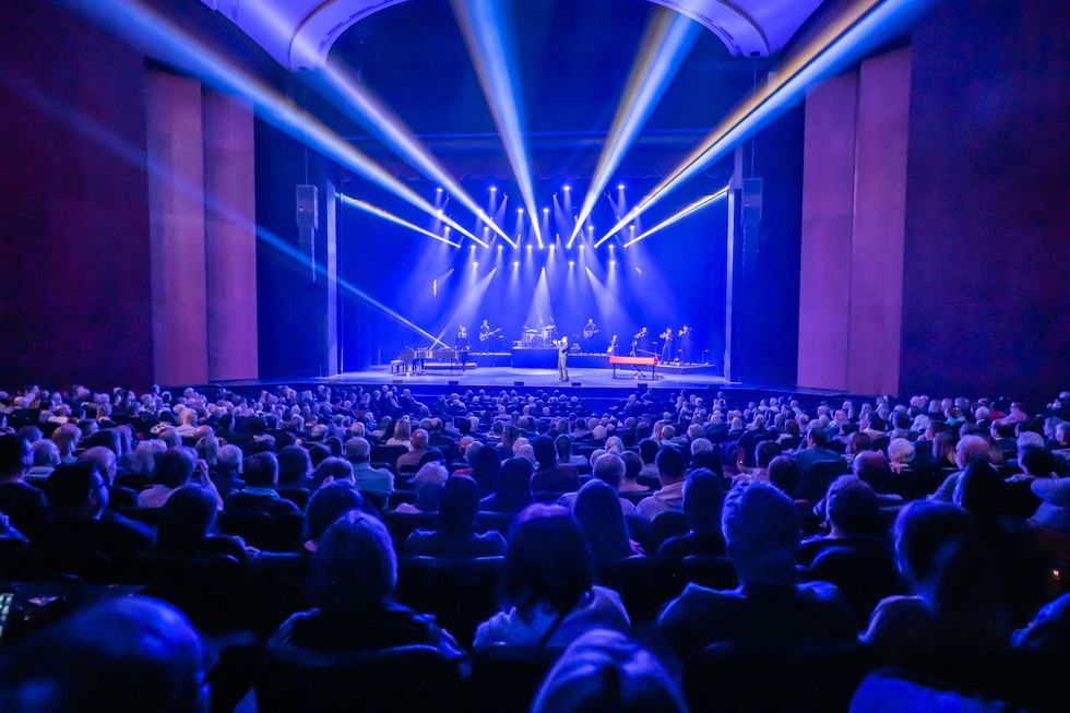 A crowd watches a performer on a lit-up theatre stage.