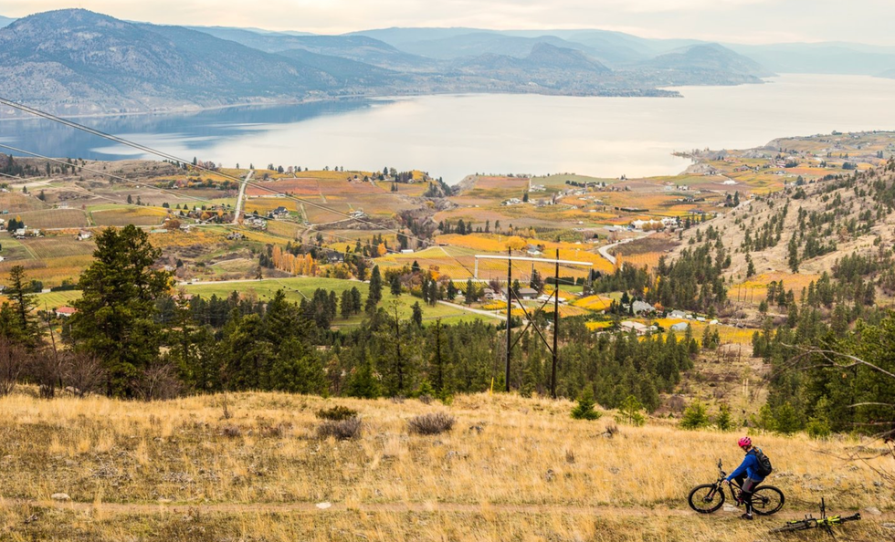 A cyclist pauses on a path overlooking the Okanagan Valley, lake and mountains.