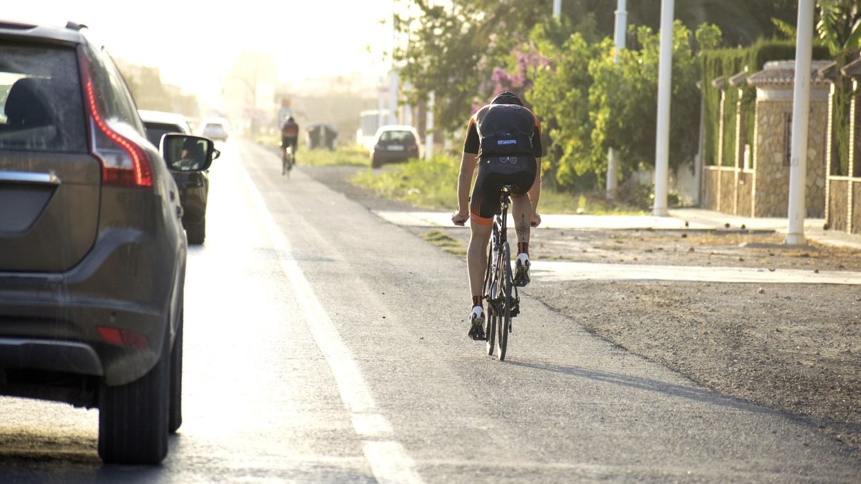 A cyclist riding a bike on the road along cars passing him.
