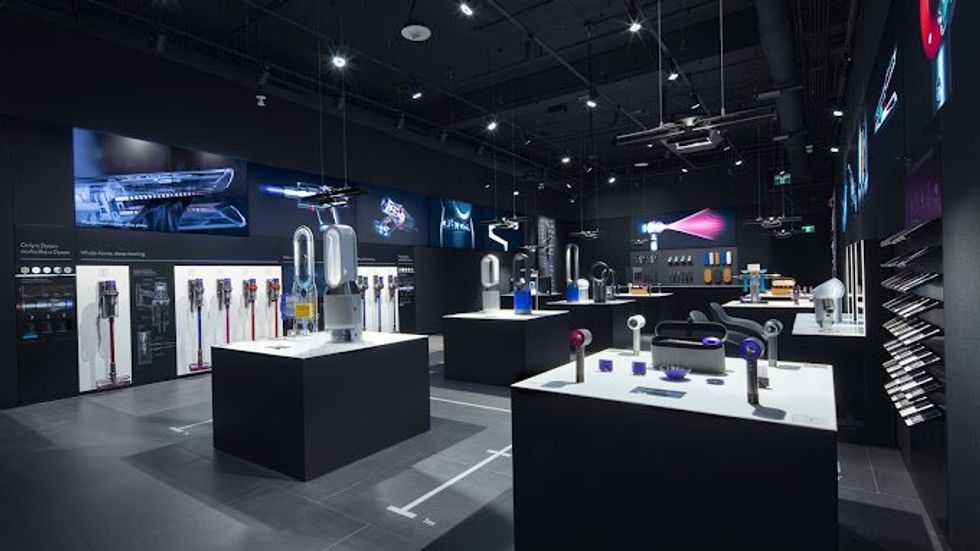 A dark shop interior dramatically lit by screens and lights to show off the Dyson products on display on panels and against the walls.