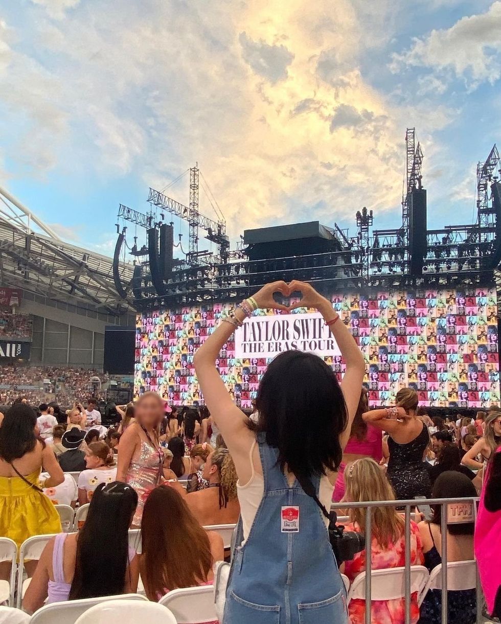 A fan makes a heart with their hands in the crowd at Taylor Swift's concert.