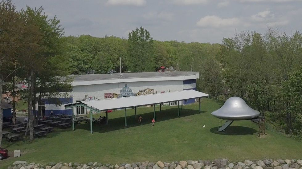 A flying saucer beside a resort building on a green field.