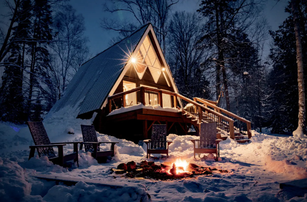 A-frame cabin covered in snow with a bonfire pit.\u200b