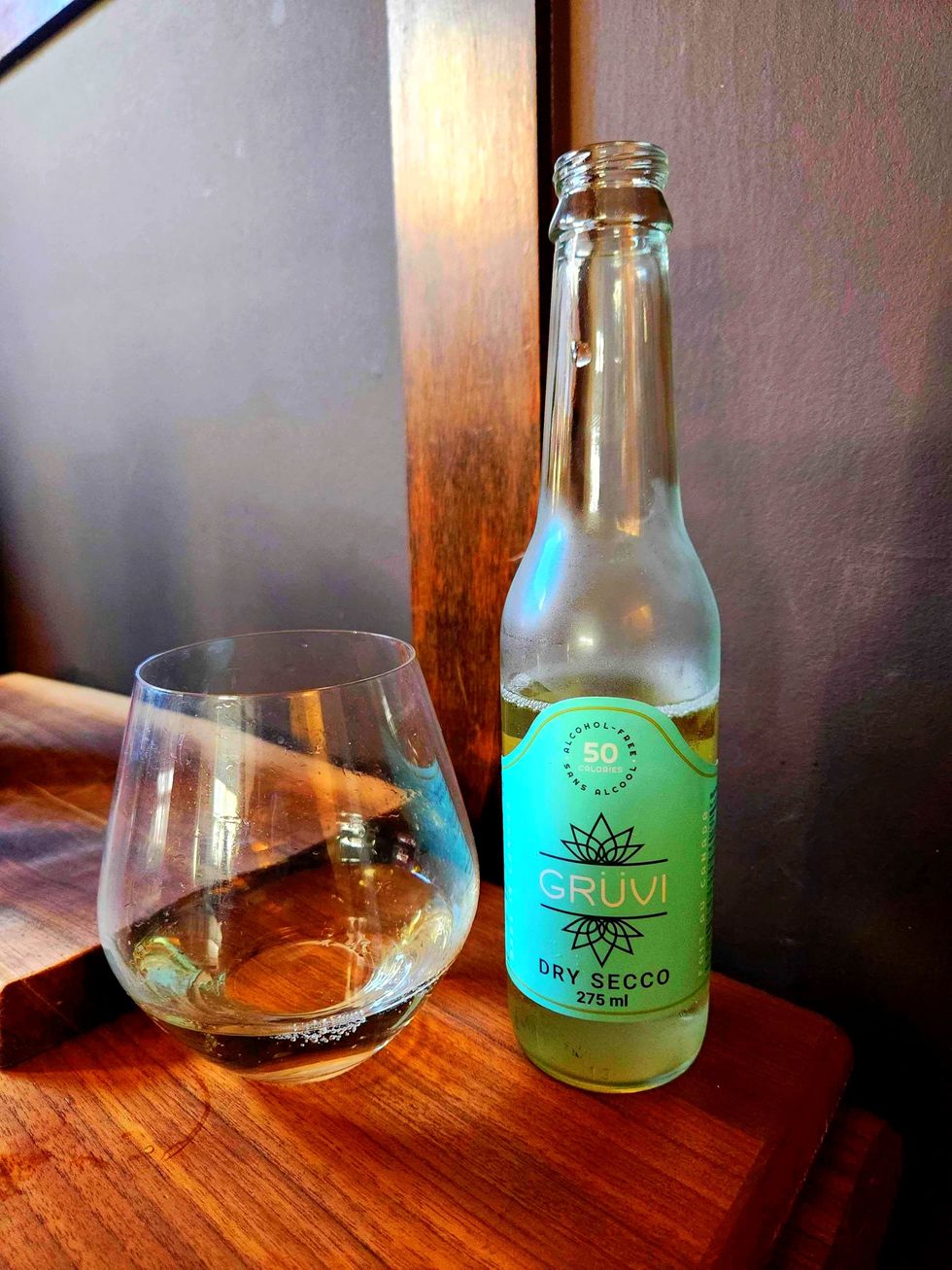 A glass of Gruvi Alcohol Free Wine Dry Secco and a bottle of Gruvi Alcohol Free Wine Dry Secco on a wooden table.