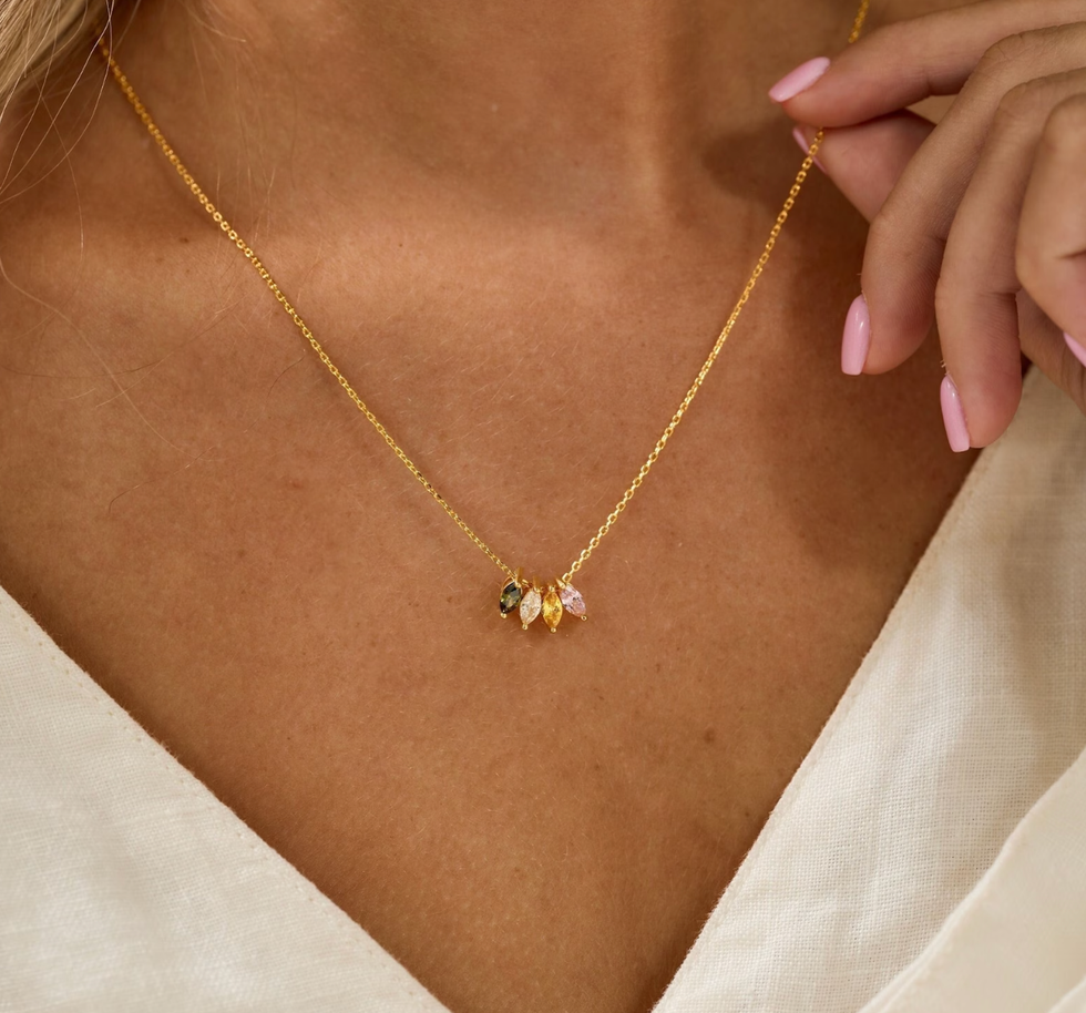 A gold necklace with multi-coloured gemstones around a woman's neck.