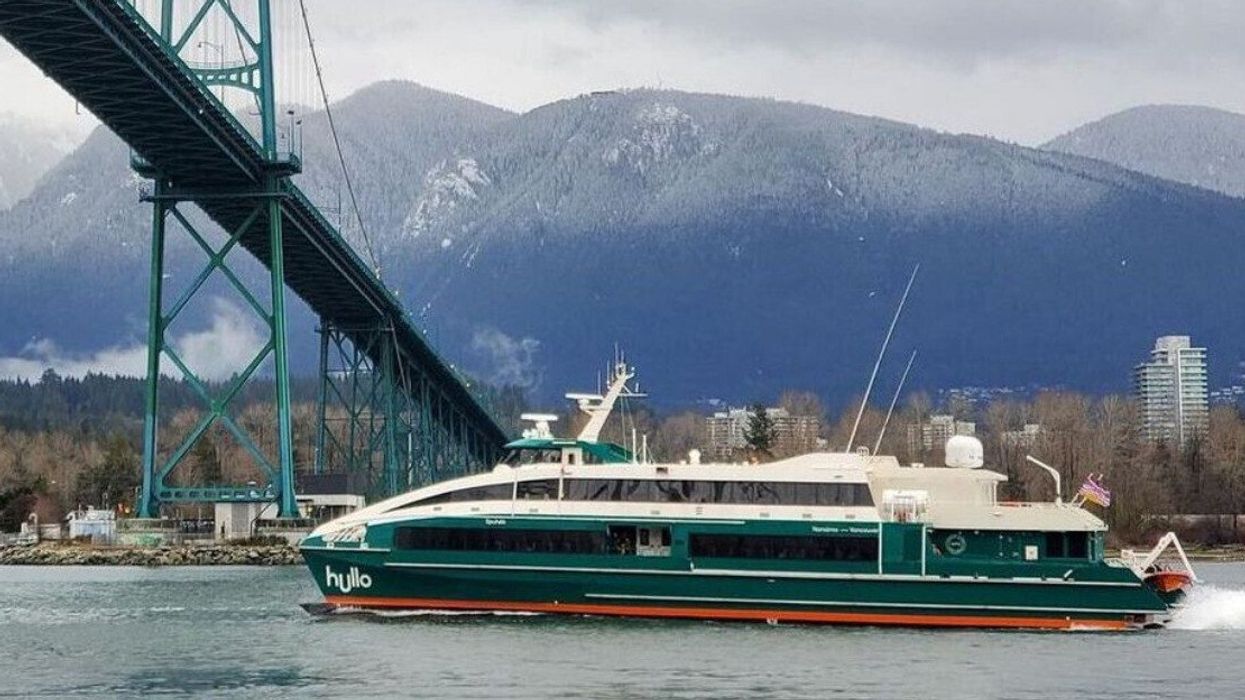 A green and white ferry sailing across the water and under a bridge.