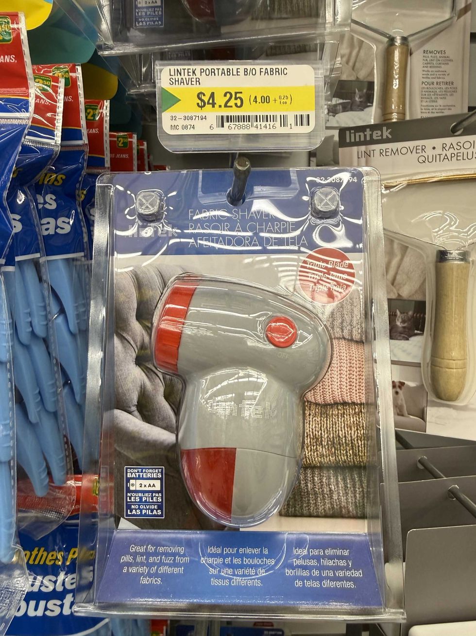 A grey and red device that has a picture of sweaters and a couch on it and label reading fabric shaver.