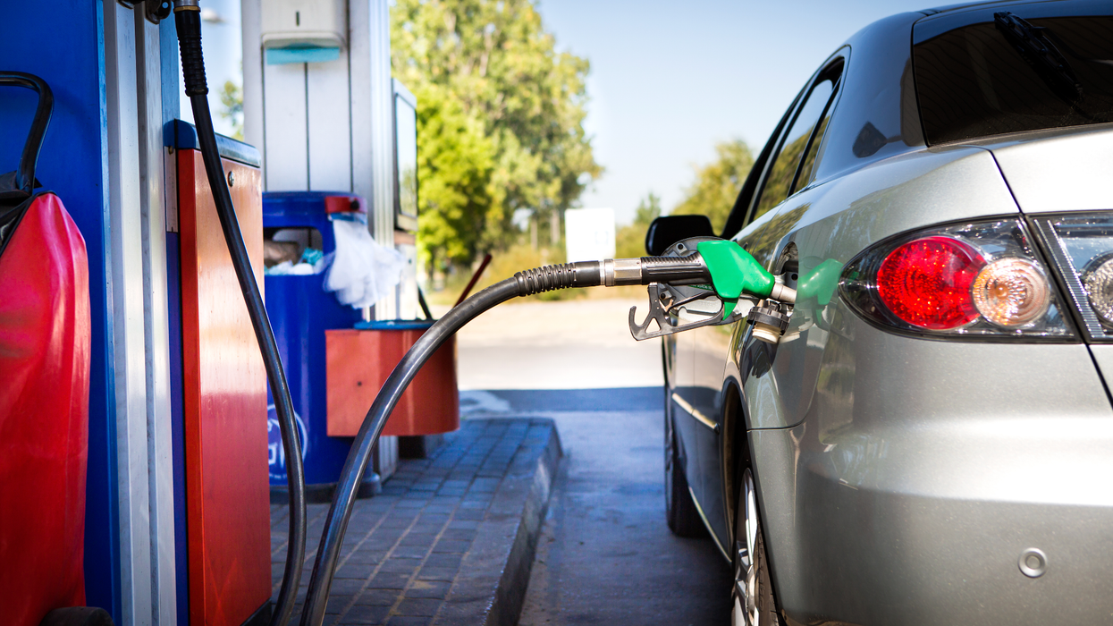 A grey car at a gas station with a pump in it, fuelling up.