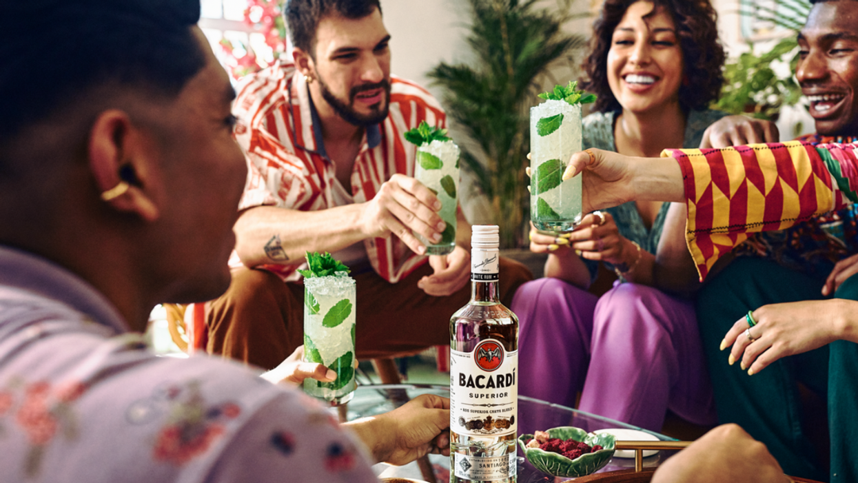 A group of friends cheers with their mojitos over a bottle of BACARDÍ Rum.