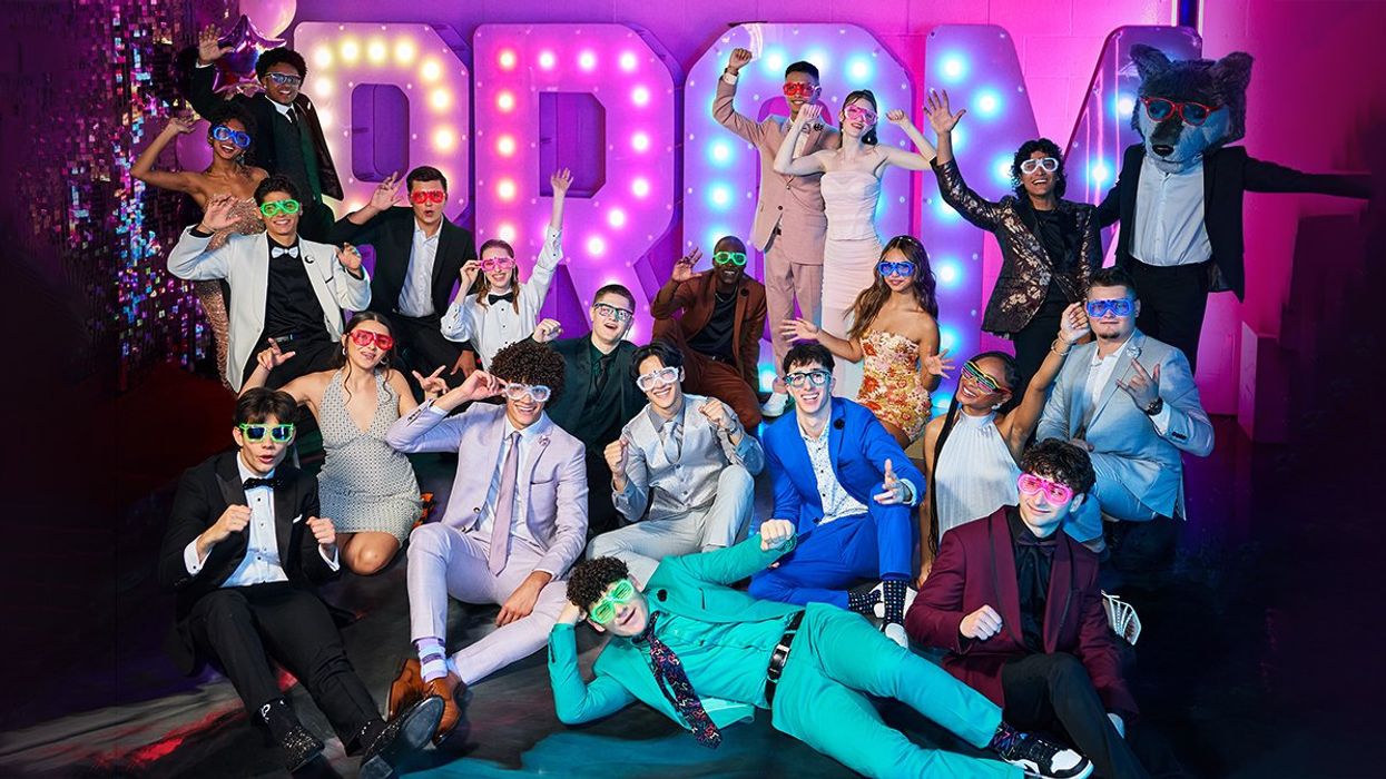 A group of high school students in colourful formalwear pose in front of a light-up sign that reads "Prom"