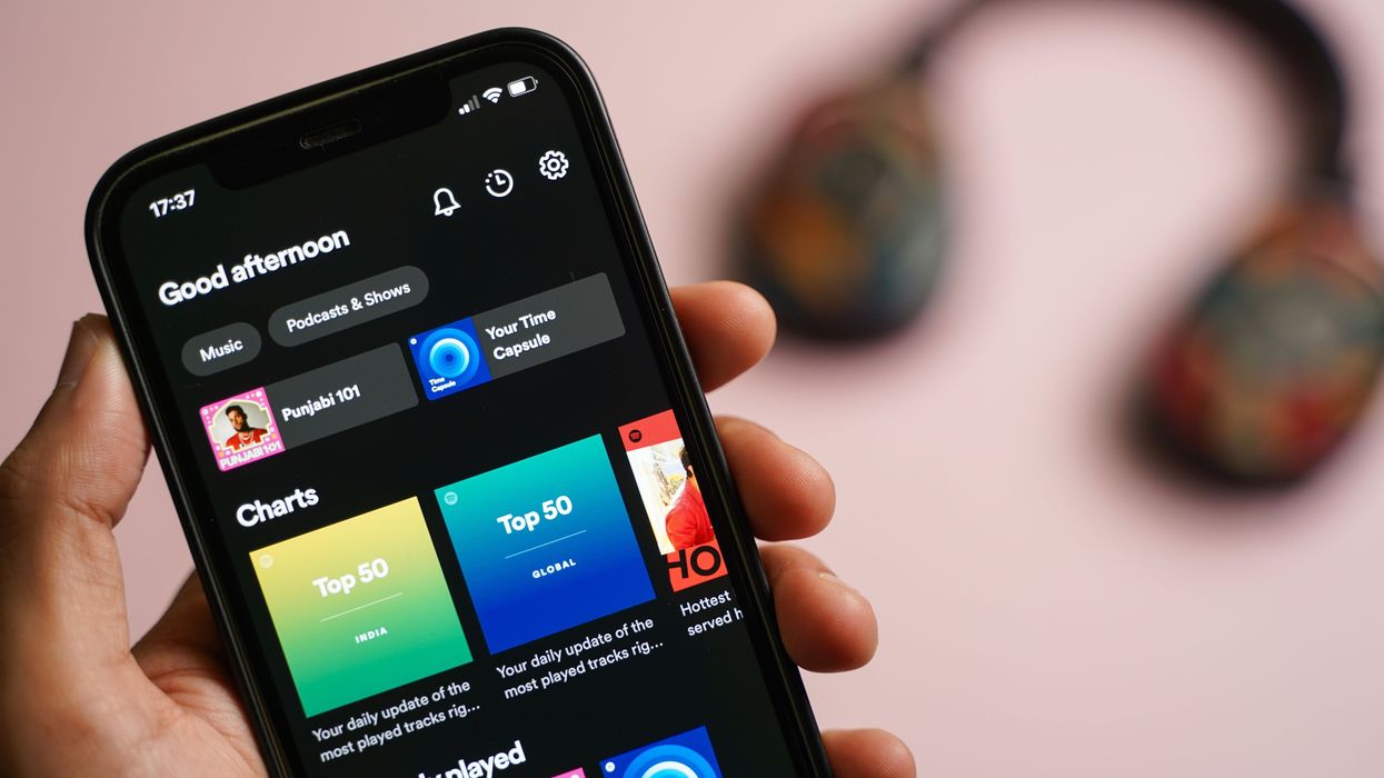 A hand holding a black smart phone with Spotify opened on it.