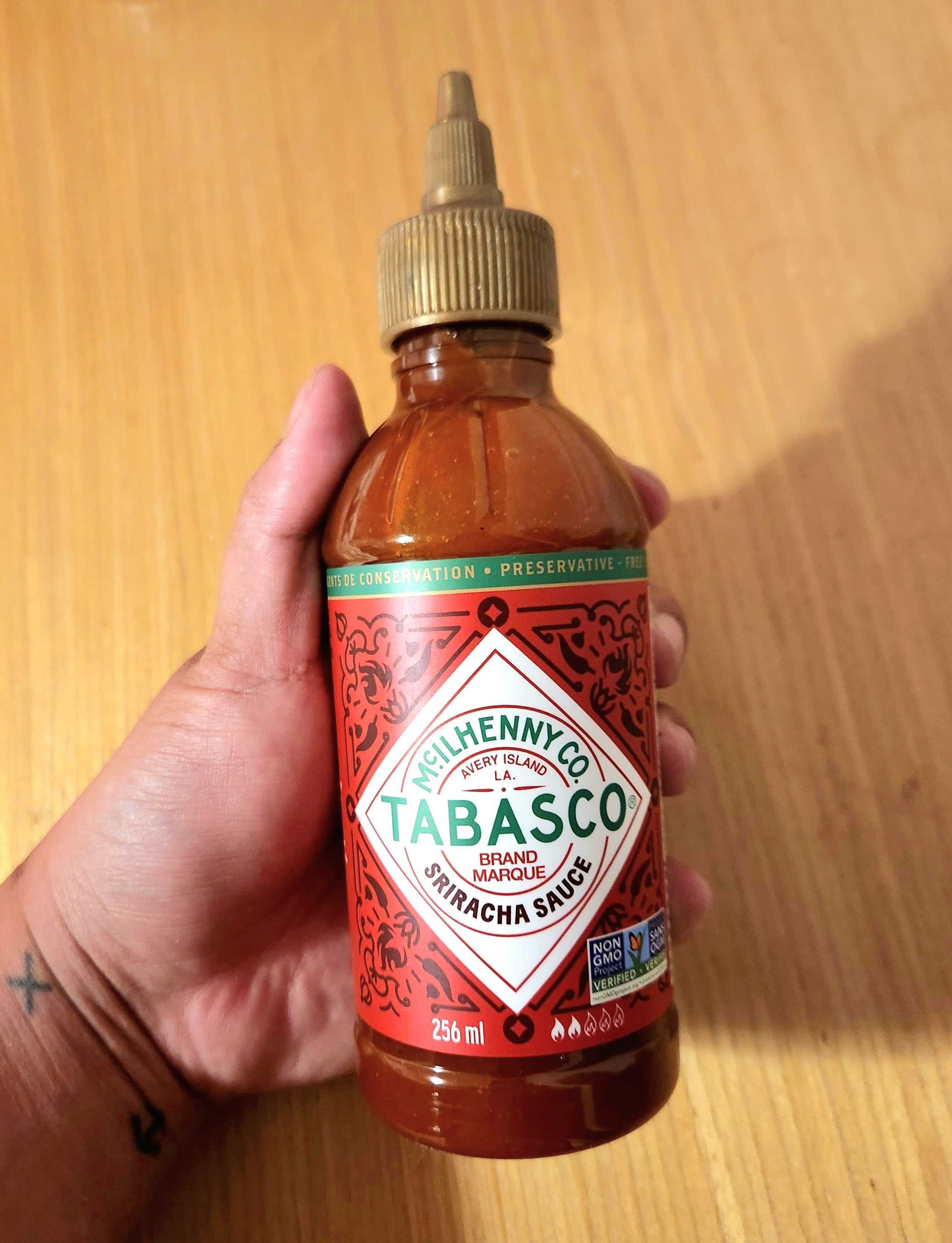 A hand holding a bottle of hot sauce with a red label and a gold cap.