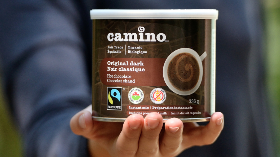A hand holding a can of Camino-branded dark hot chocolate mix.