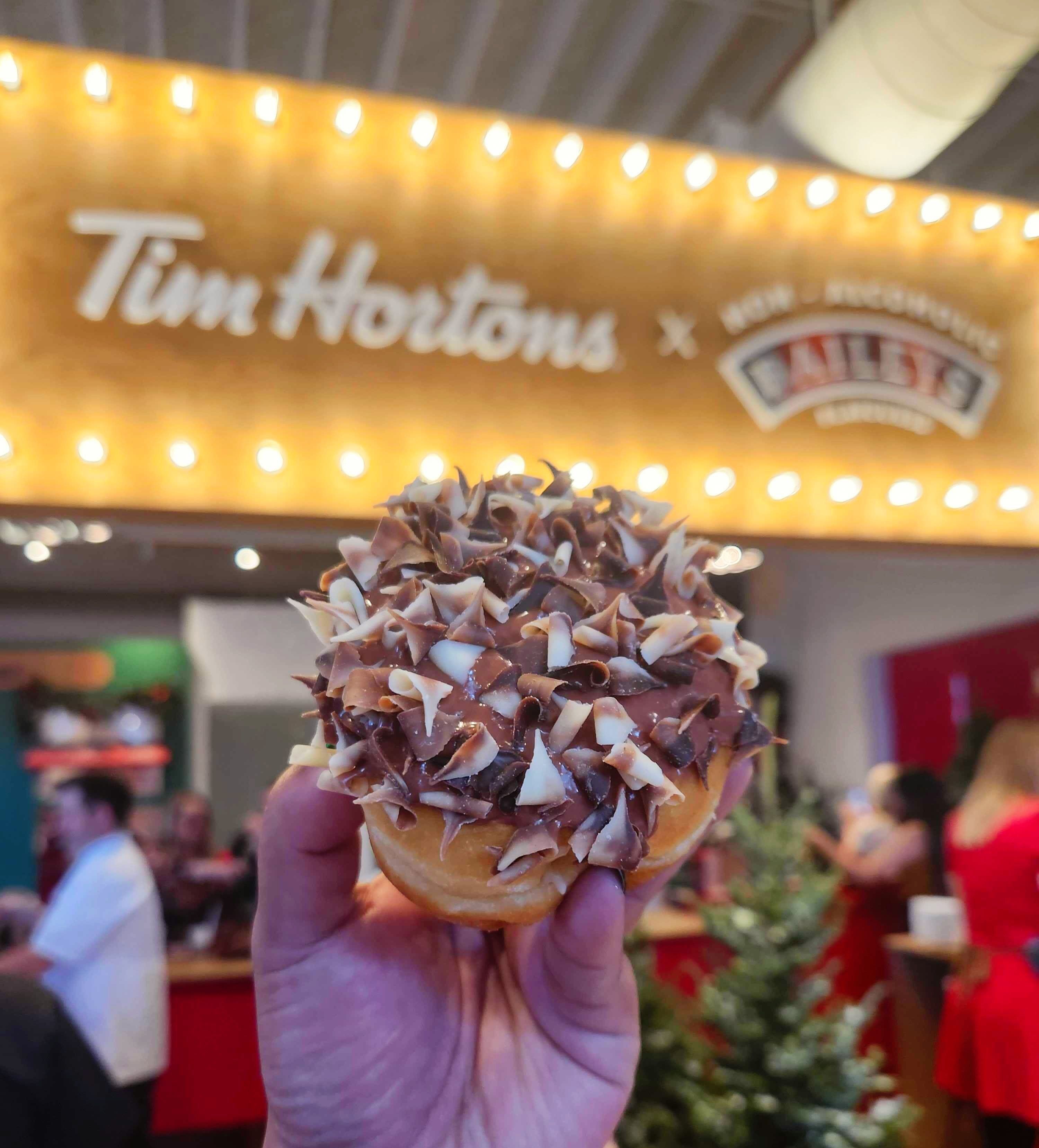 A hand holding a doughnut with white and brown chocolate flakes and brown chocolate icing.