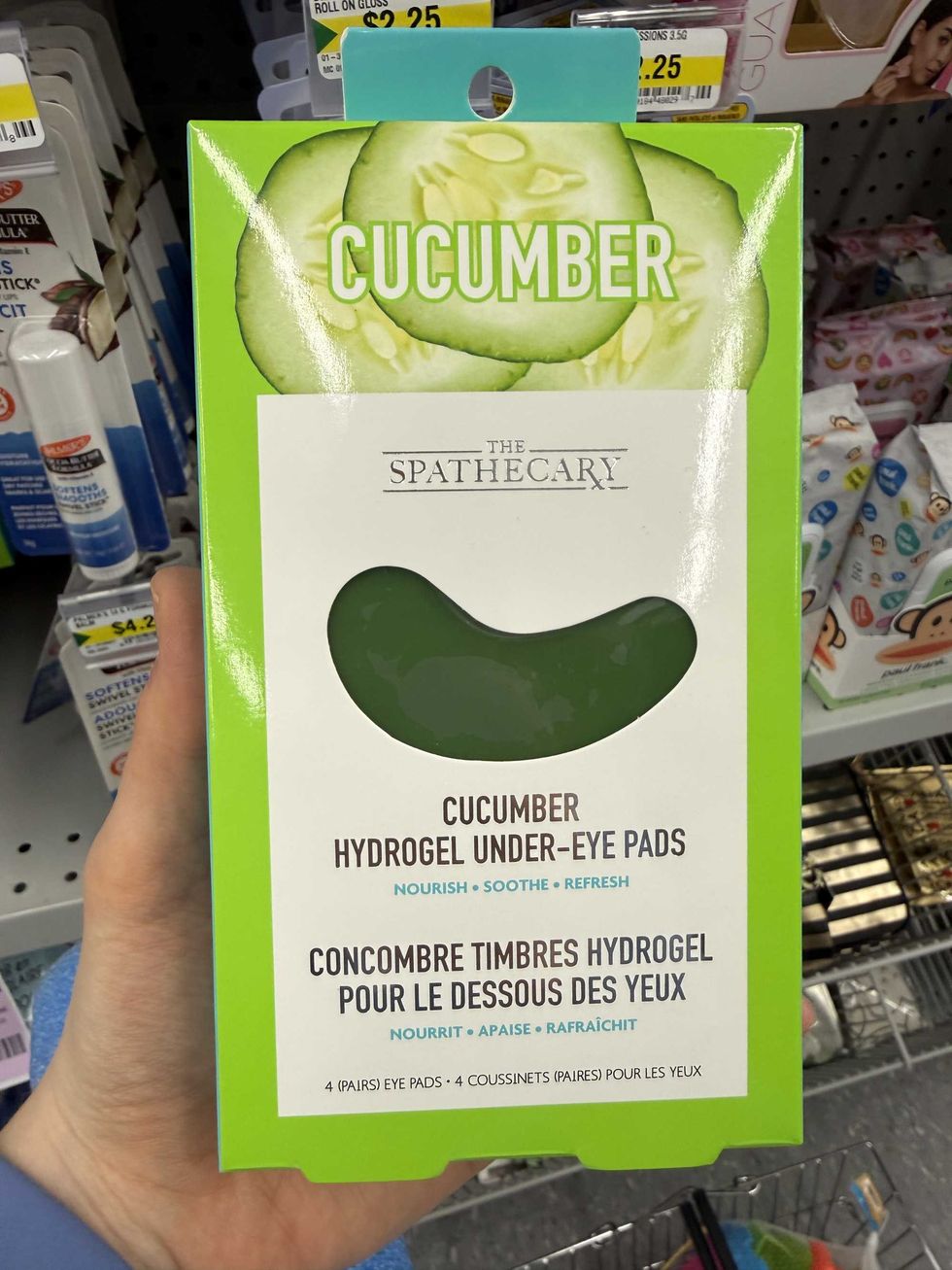 A hand holding a green and white box that says Cucumber Hydrogel Under-Eye Pads.