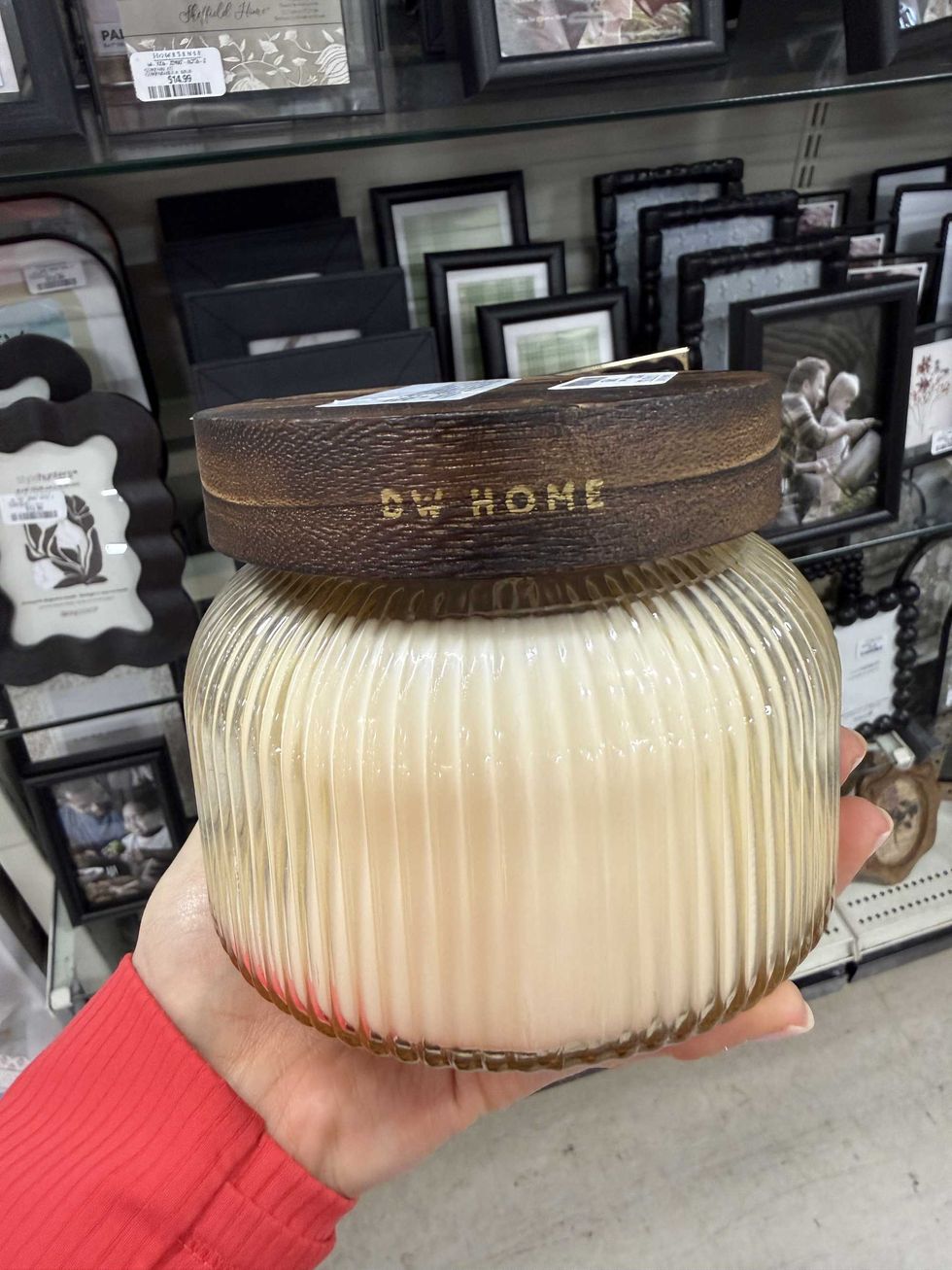A hand holding a large candle in a glass container with a brown lid.