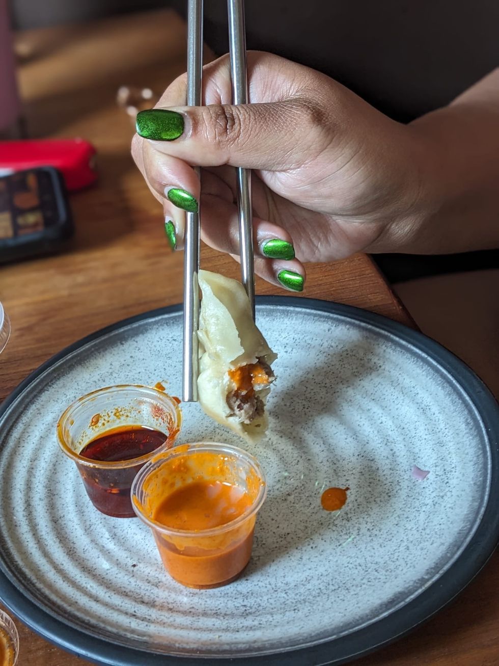 A hand holding a momo in chopsticks.