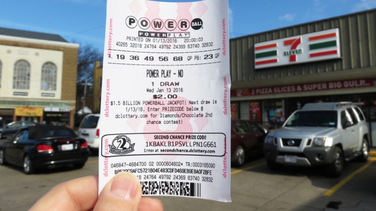 A hand holding a Powerball lottery ticket in front of a 7 Eleven.