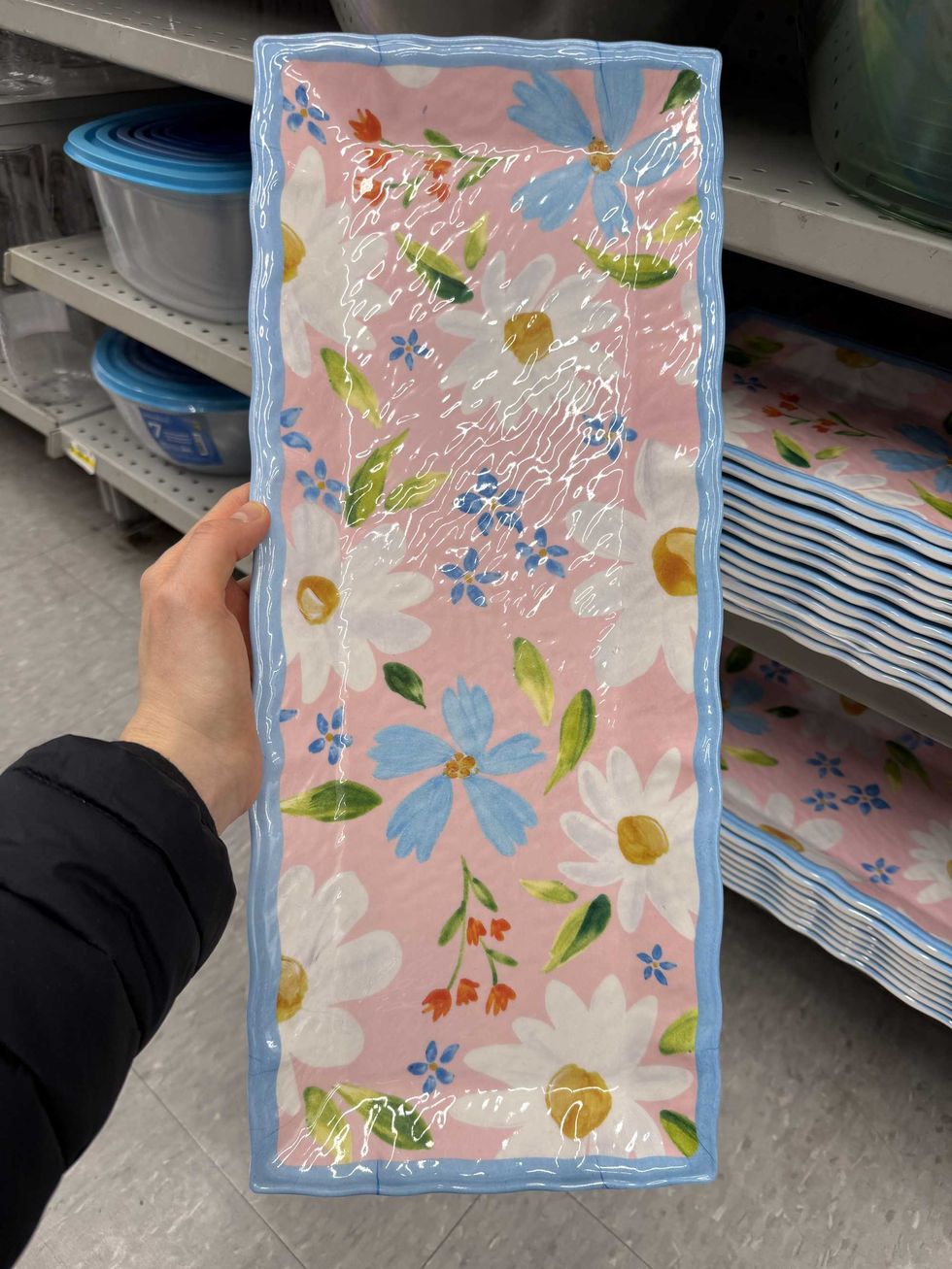A hand holding a rectangular serving platter with colourful flowers on it.