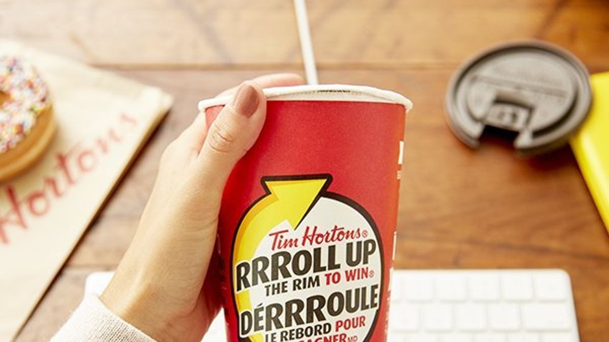 A hand holding a red Tim Hortons cup with the rim being rolled up.
