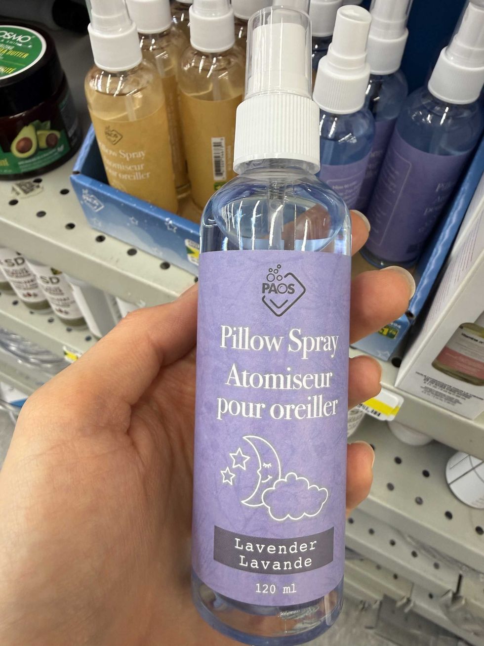 A hand holding a spray bottle with a purple label that has a moon and cloud on it that says pillow spray lavender.