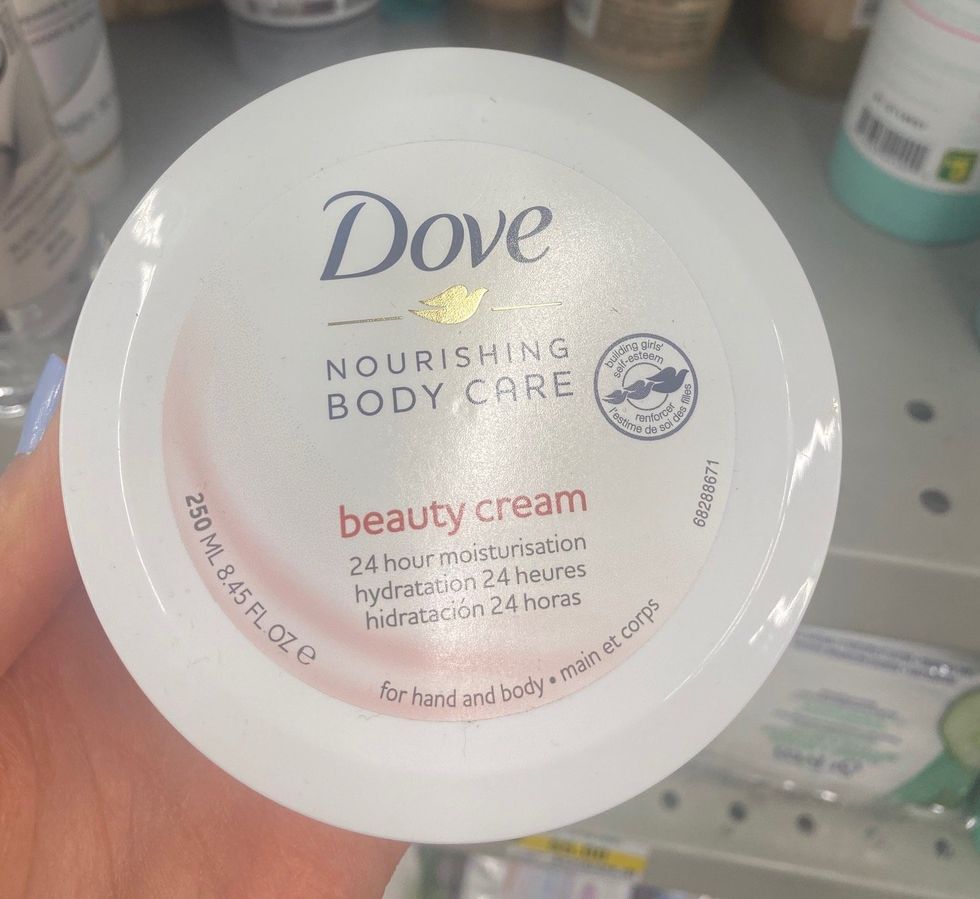 A hand holding a tub of body cream at a store,