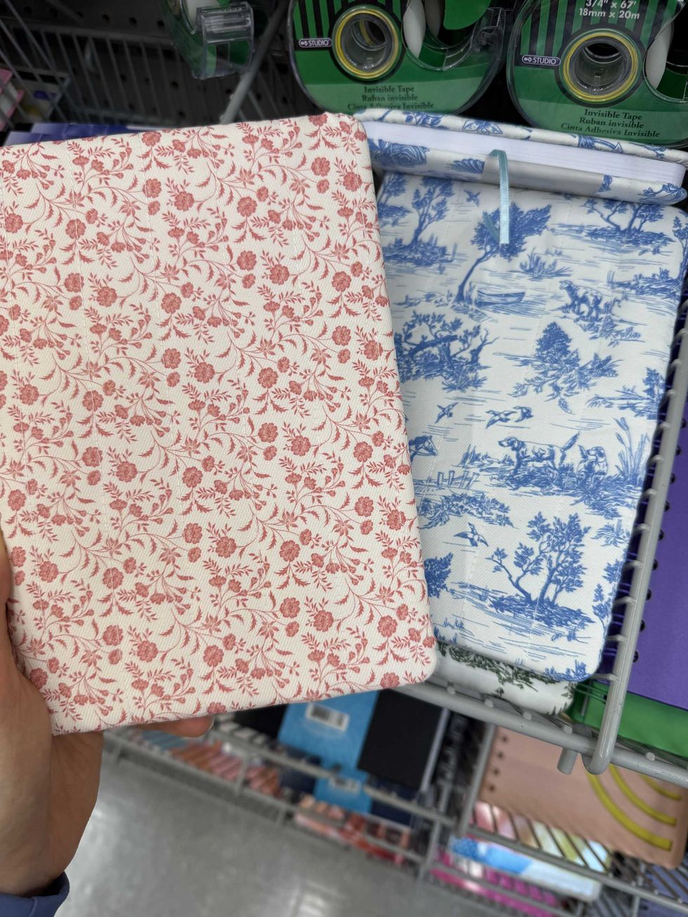 A hand holding a white notebook with red flowers on it.