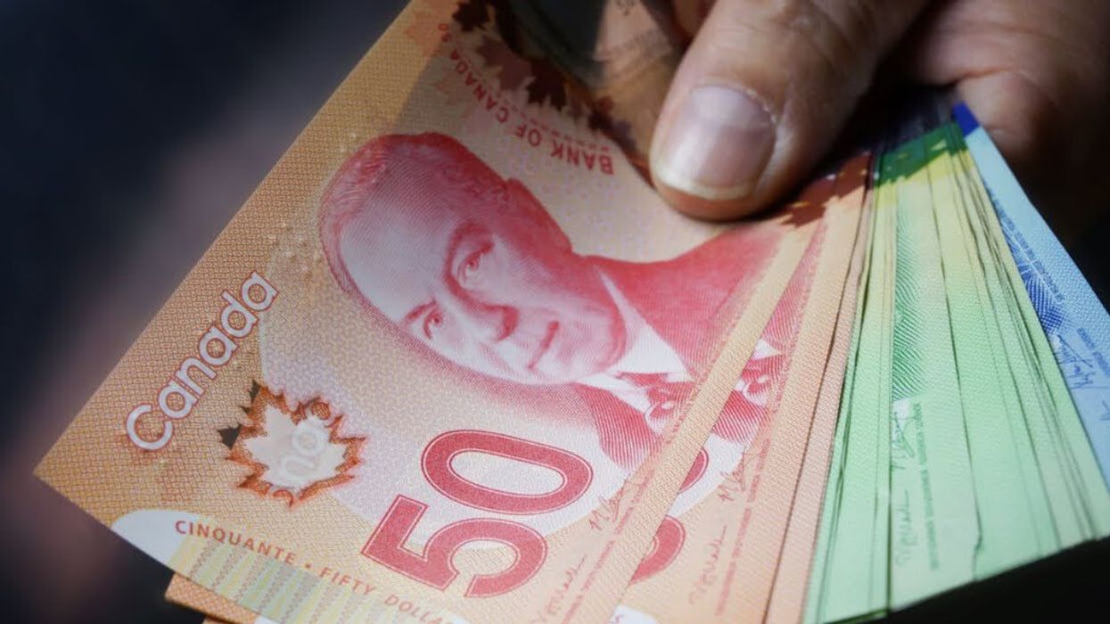 A hand holding Canadian fifty, twenty and ten-dollar notes.