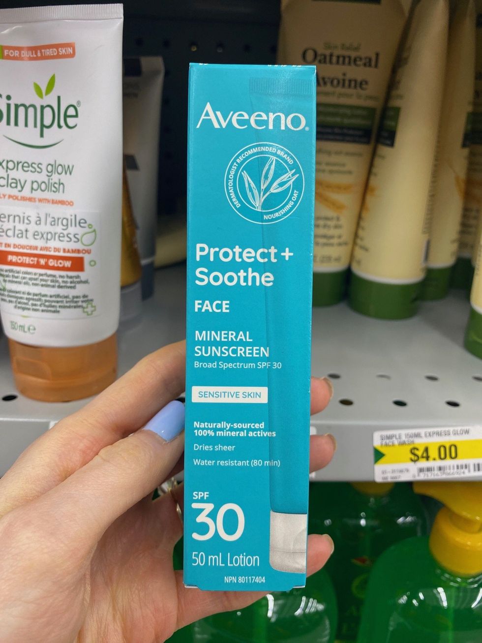 A hand holding sunscreen on sale in a store.