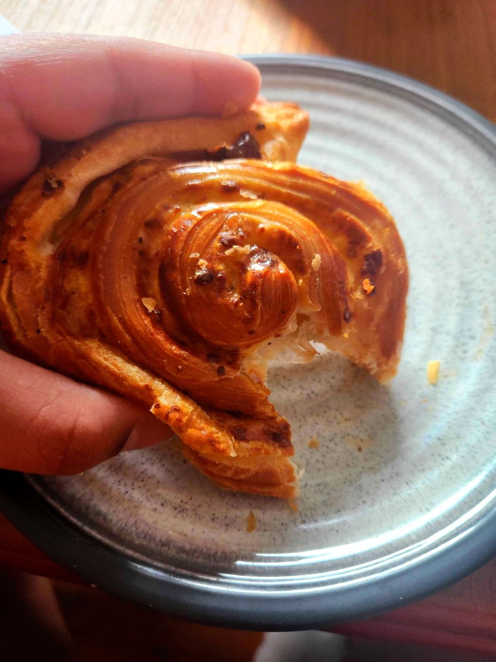 A hand holding the Caramelized Onion and Parmesan Savoury Pinwheel on a plate.