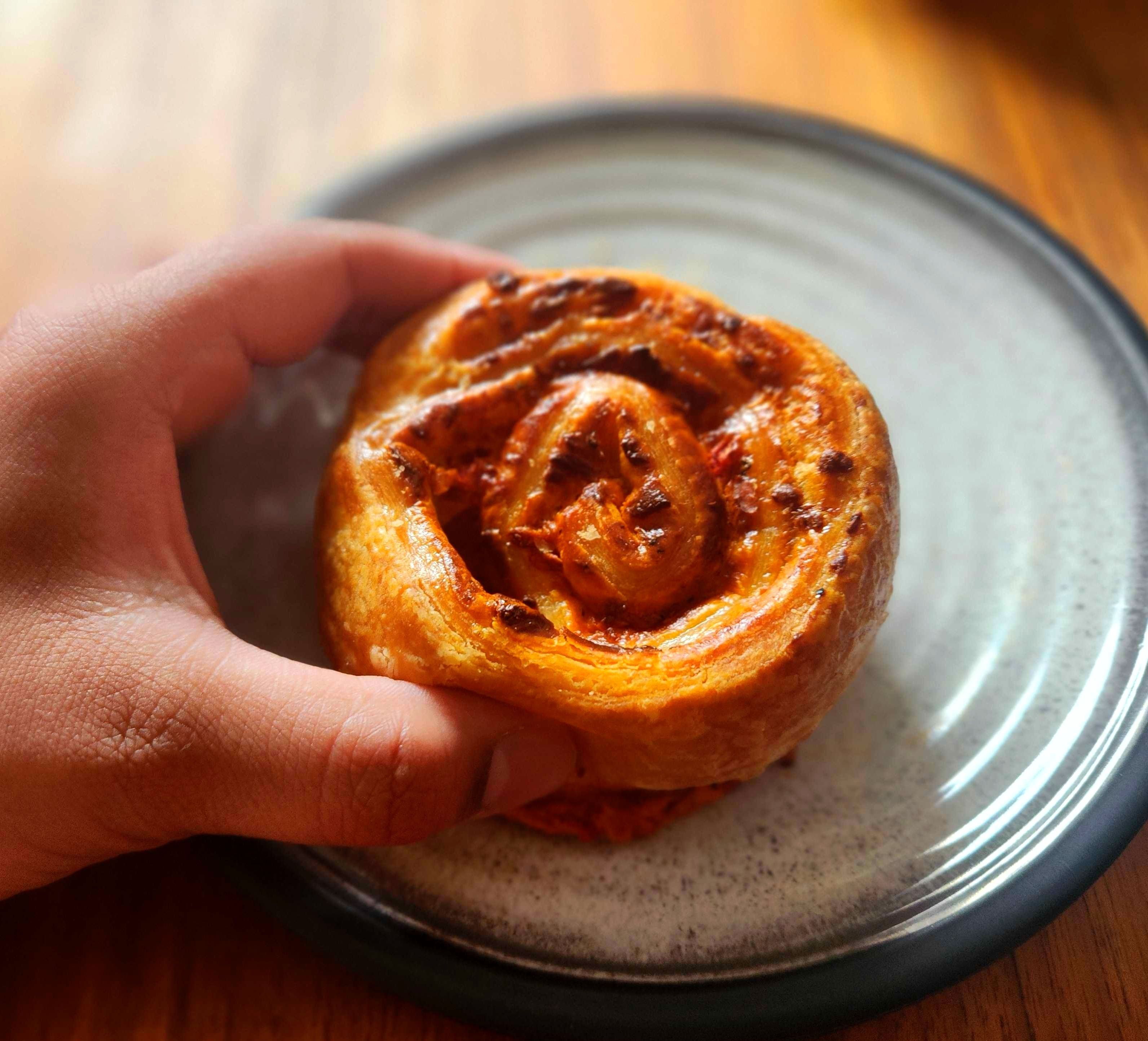 A hand holding The Roasted Red Pepper and Swiss Savoury Pinwheel on a plate.