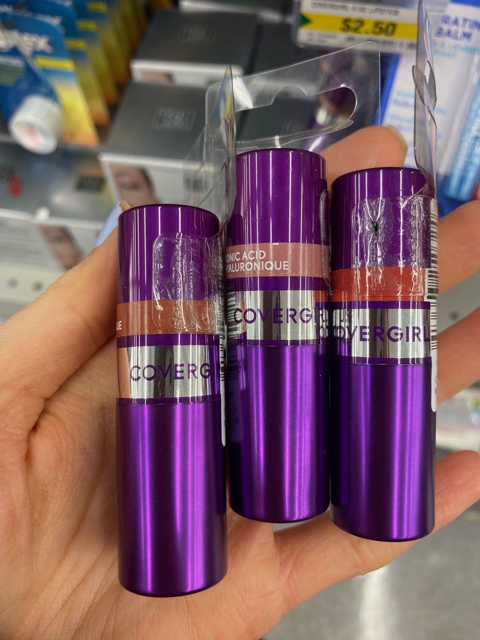 A hand holding three tubes of lipstick.