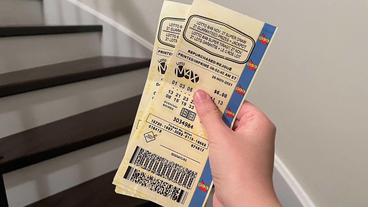 A hand holding two Lotto Max tickets.