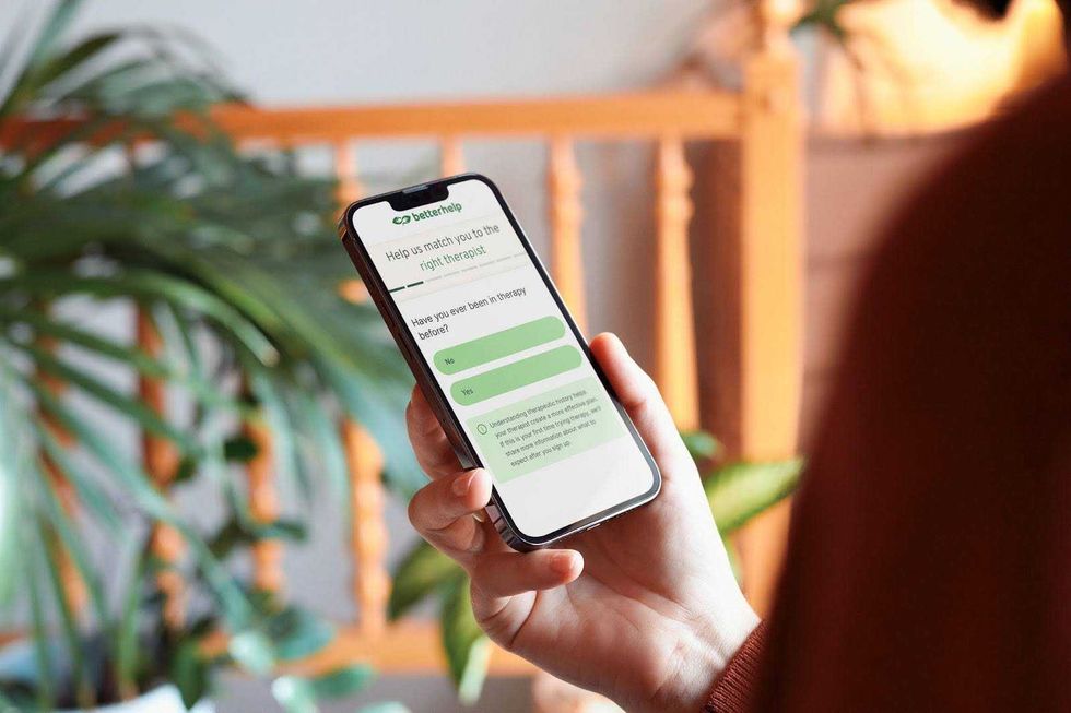 A hand holds a mobile phone displaying the therapist matching quiz on BetterHelp.