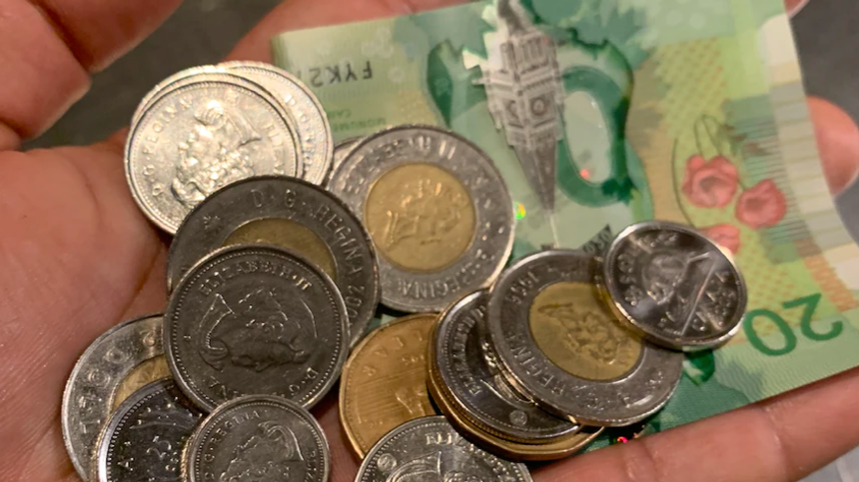 A hand holds Canadian coins and banknotes.
