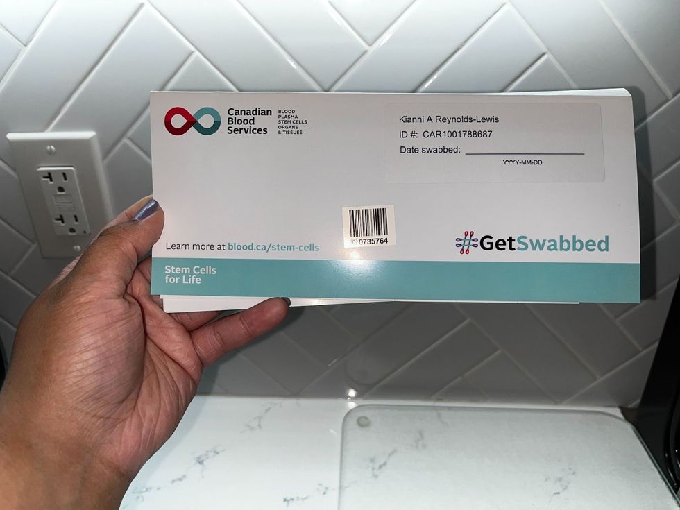 A hand holds the envelope for a stem cell swab kit up to the camera. 