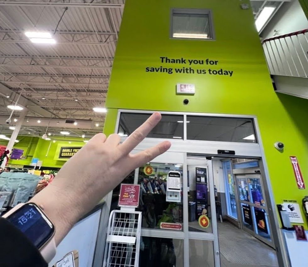 A hand holds up a "peace" sign in front of the FreshCo exit, the sign above which reads "Thank you for saving with us today."