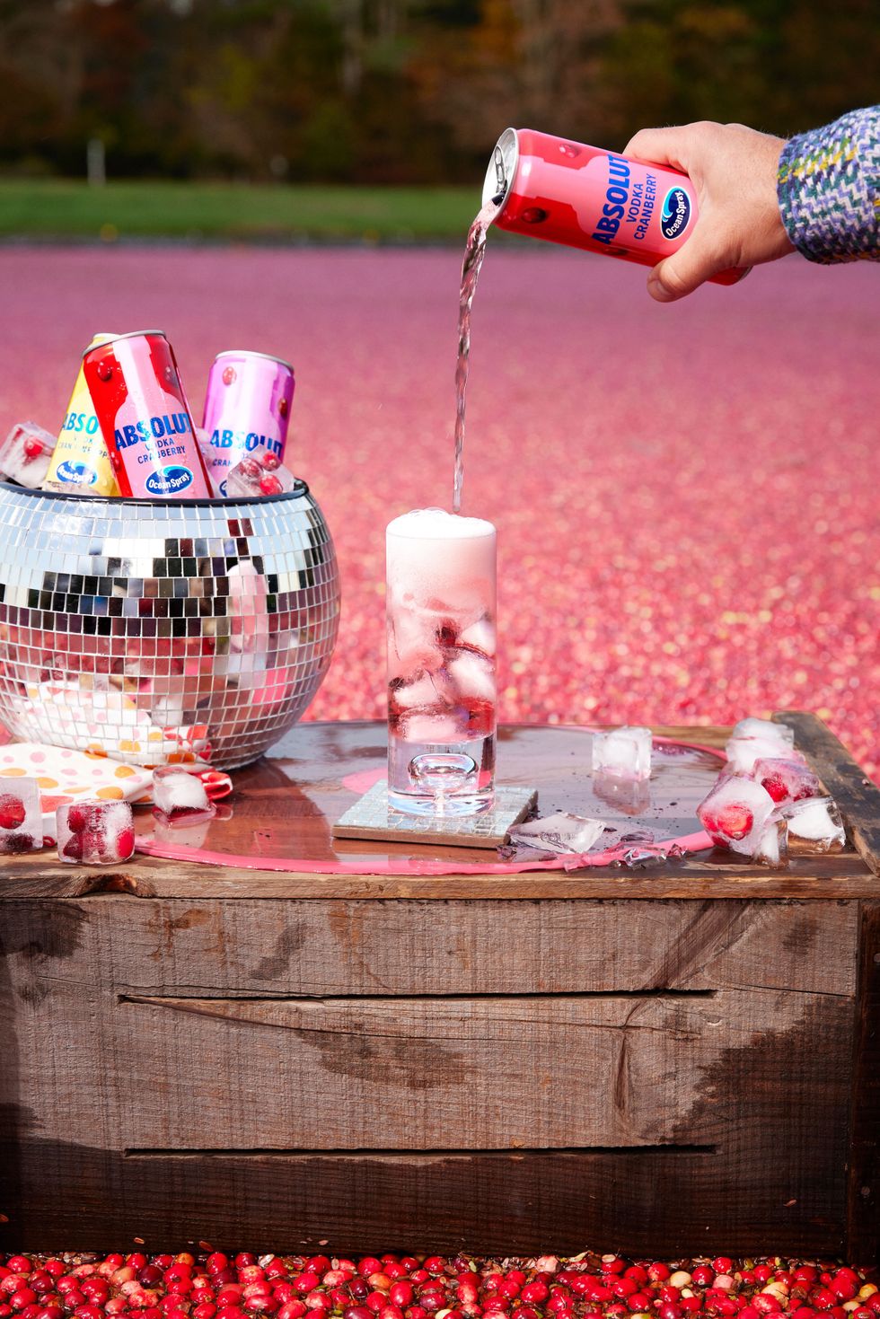 A hand pours sparkling Absolut + Ocean Spray vodka cran into a glass.