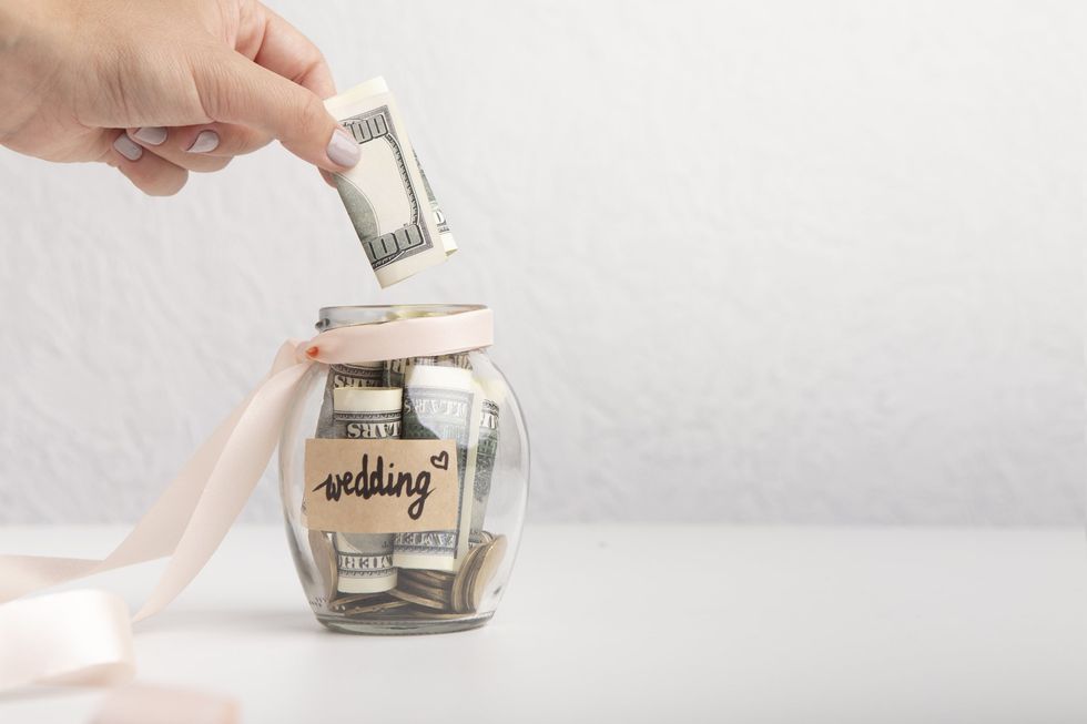 A hand putting cash into a "wedding" jar.
