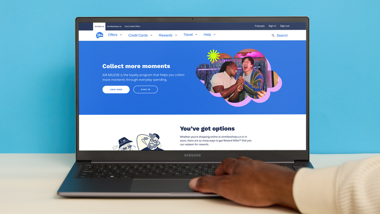 A hand scrolls the new AIR MILES site on a laptop.