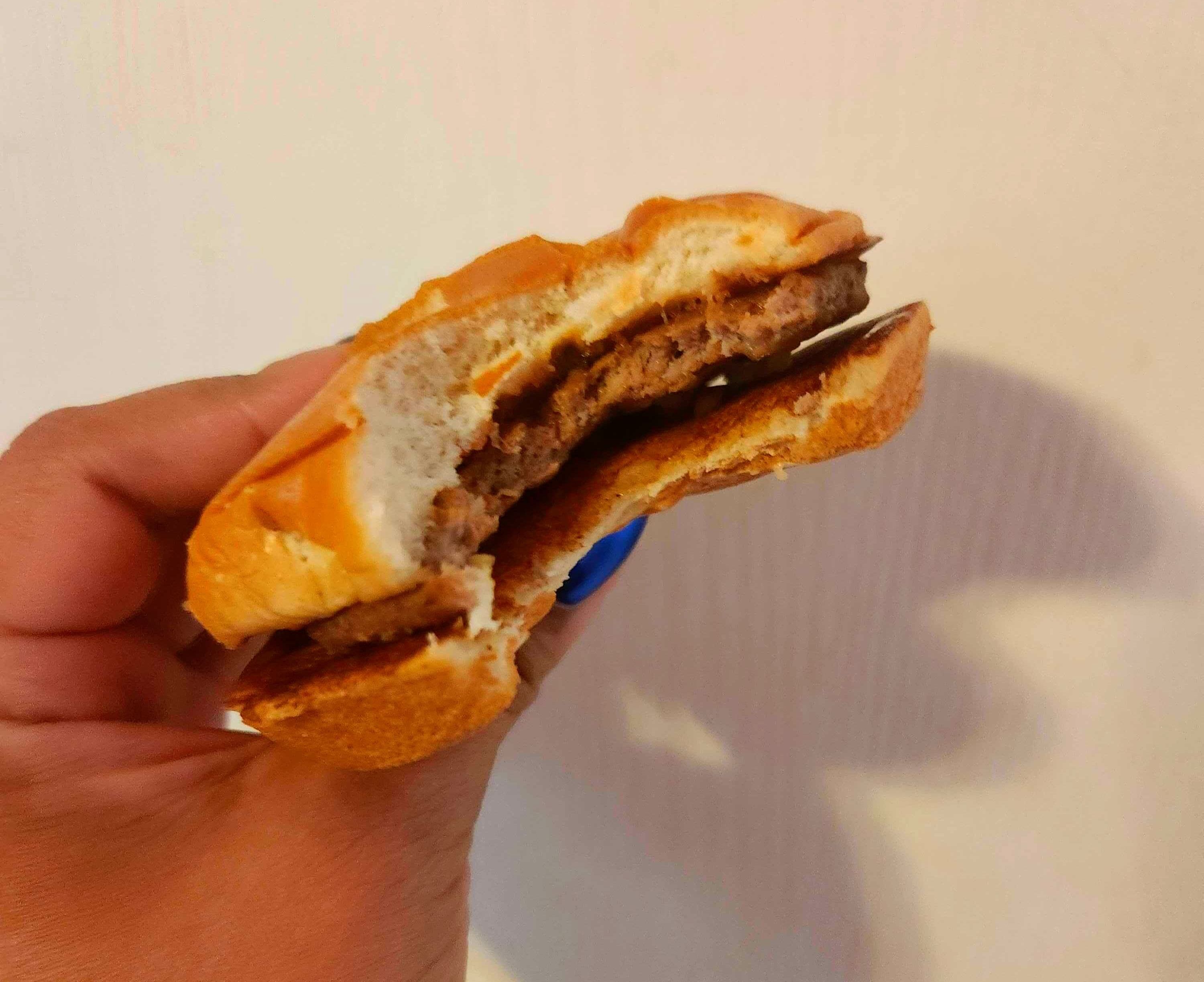 A hand with blue nail polish holding a hamburger against a white wall.