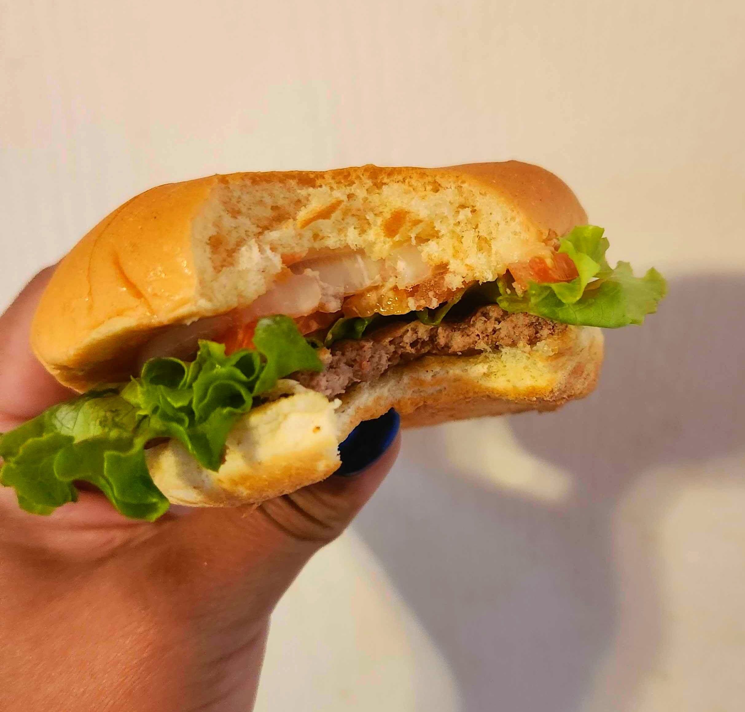 A hand with blue nail polish holding a hamburger against a white wall.