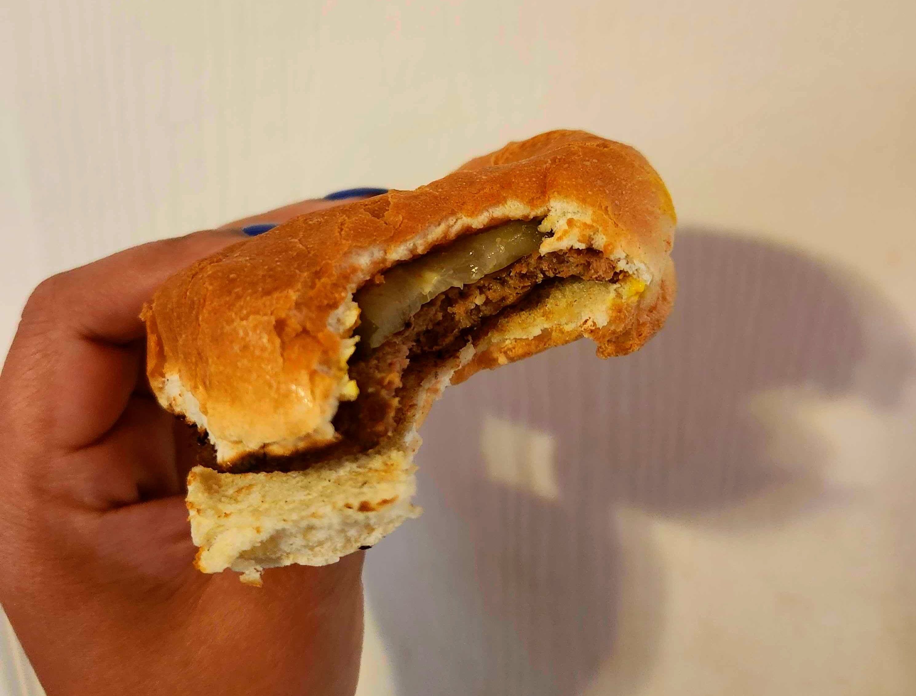 A hand with blue nail polish holding a hamburger against a white wall.