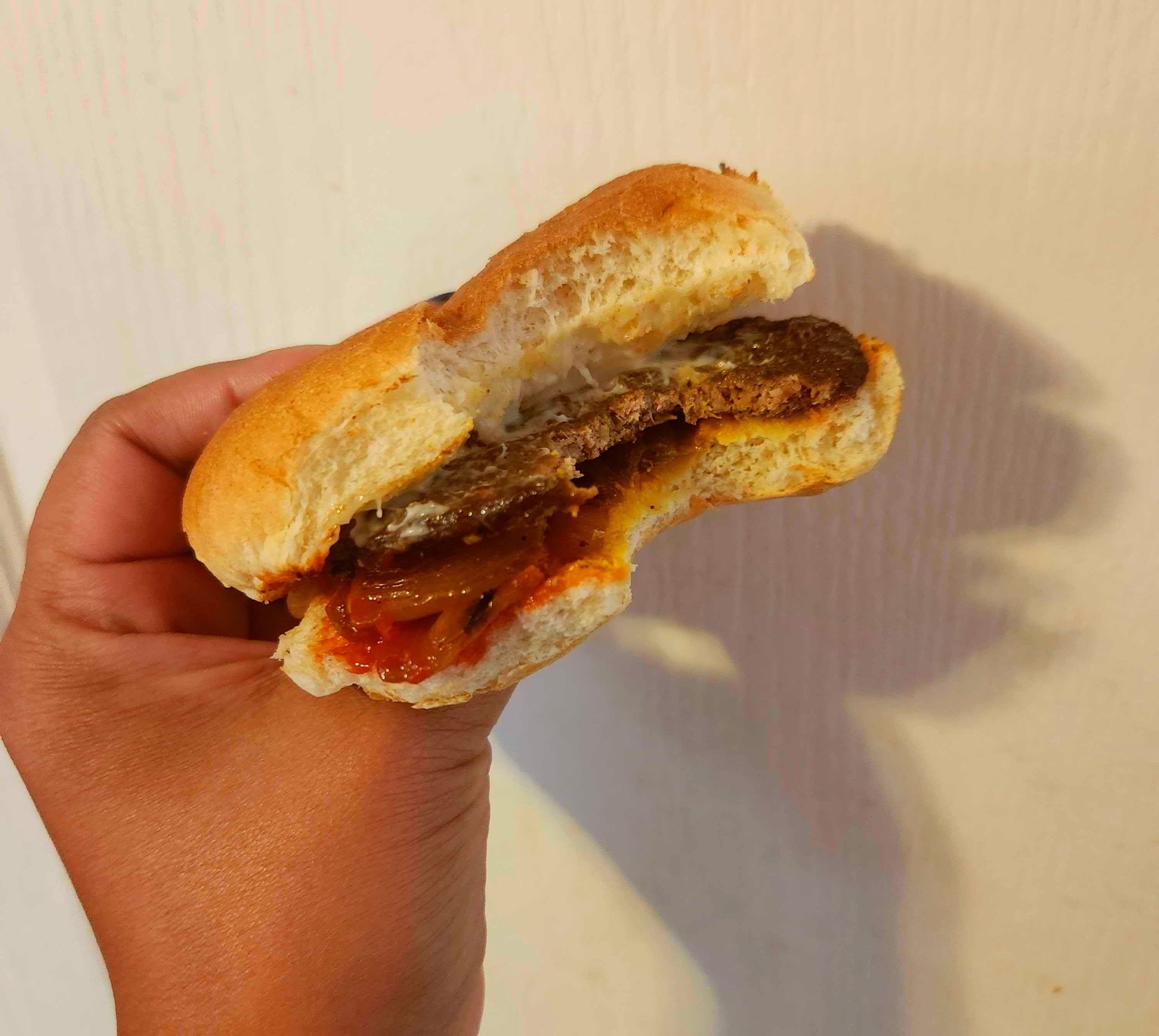 A hand with blue nail polish holding a hamburger against a white wall.