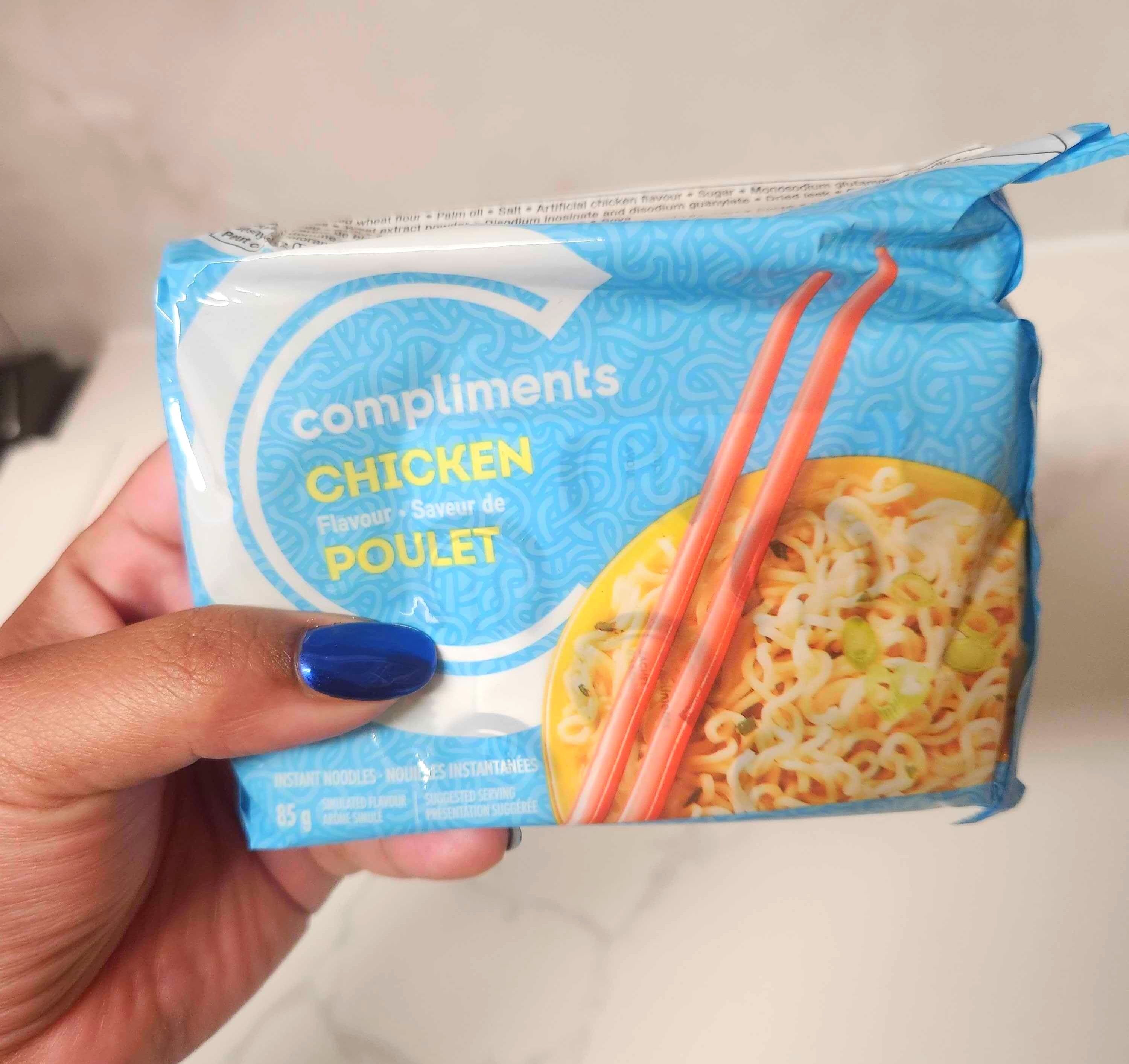 A hand with blue nails holding a blue package of soup against a marble counter .