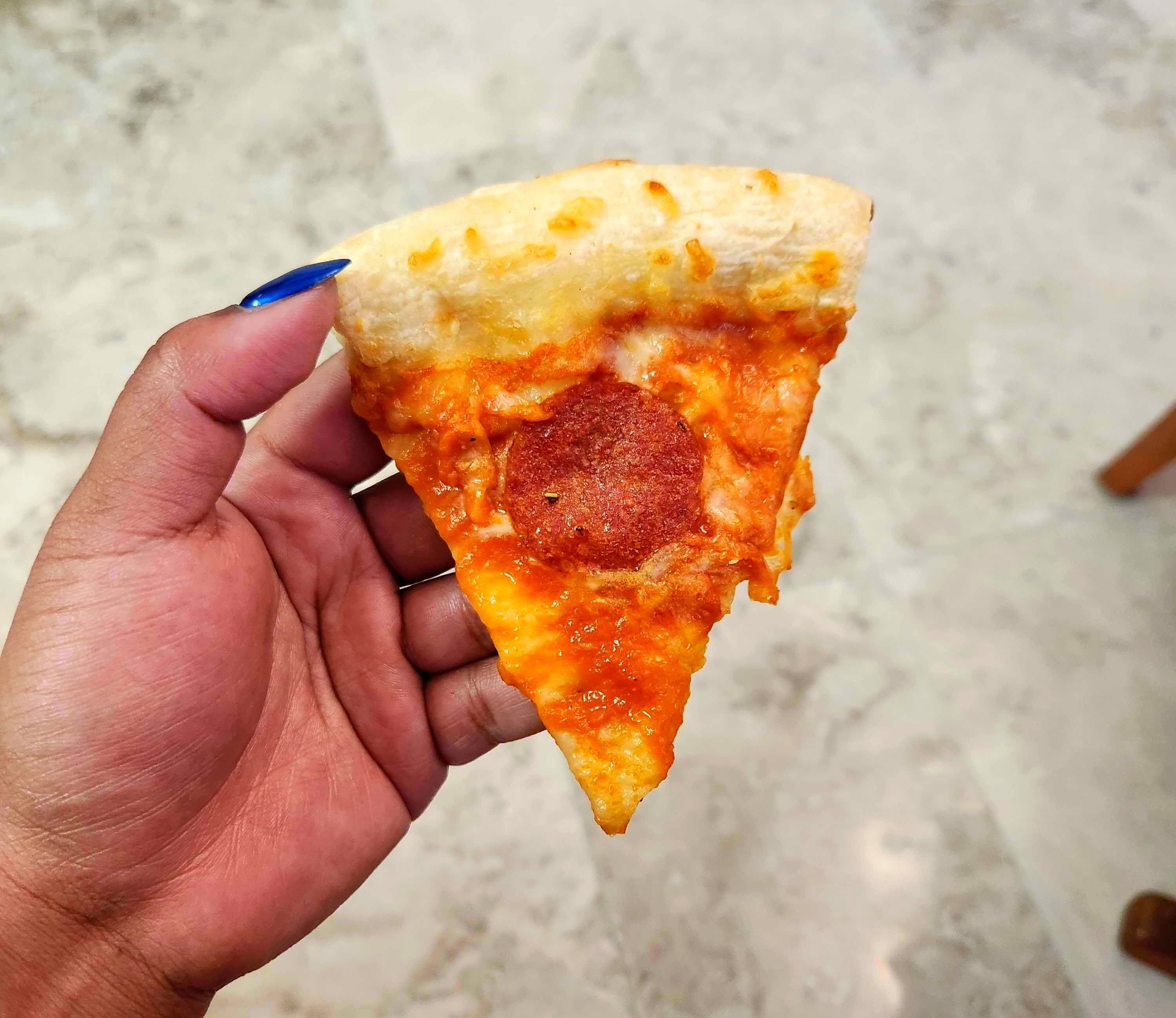 A hand with blue nails holding a slice of pizza against a tile background.